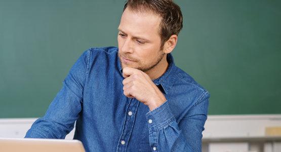 Male teacher sitting at desk staring pensively at laptop