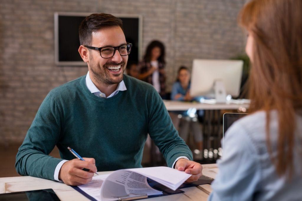 job interviewer smiling holding paper and pen facing candidate